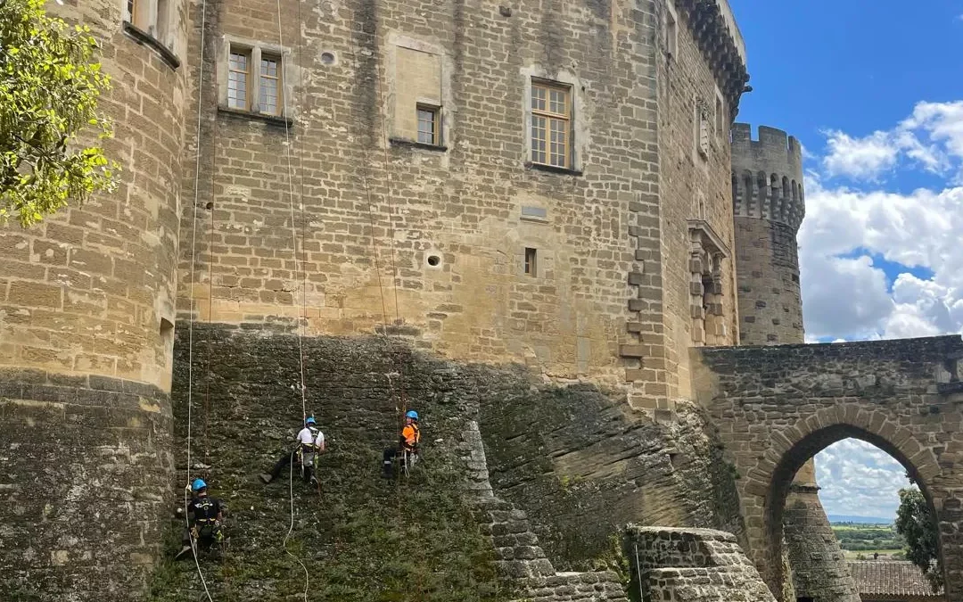 Cordistes en rappel sur les remparts d’un château fort, chantier école de dévégétalisation