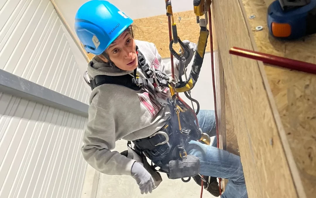 Stagiaire souriante, casque bleu, en harnais pendant l’atelier zinguerie sur cordes
